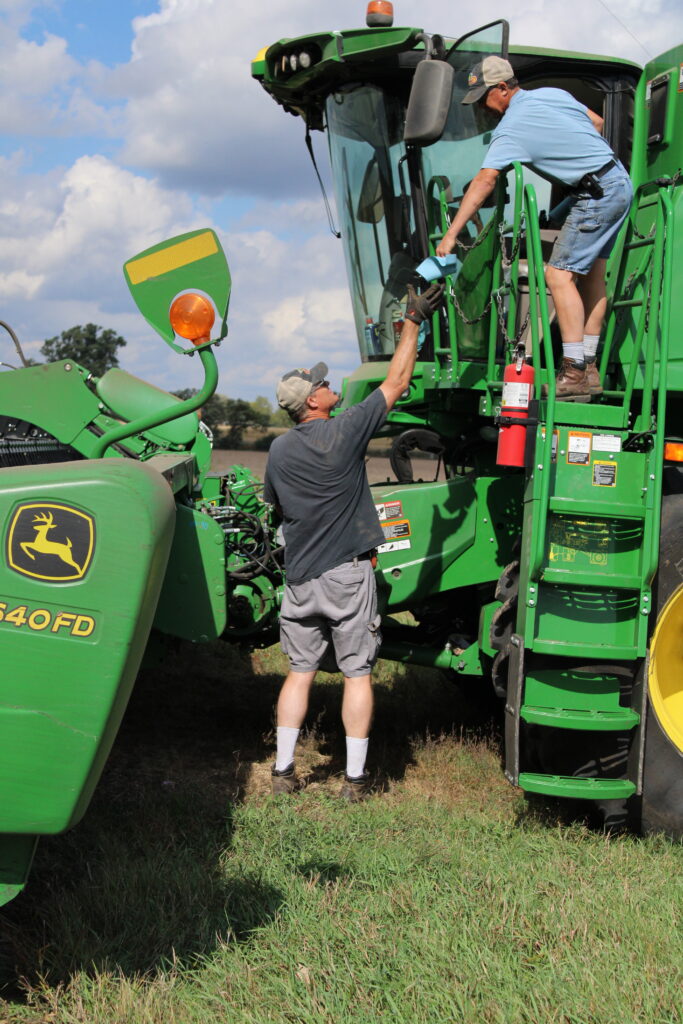 Scott Nelson hands Larry Nelson a rag to clean the combine.