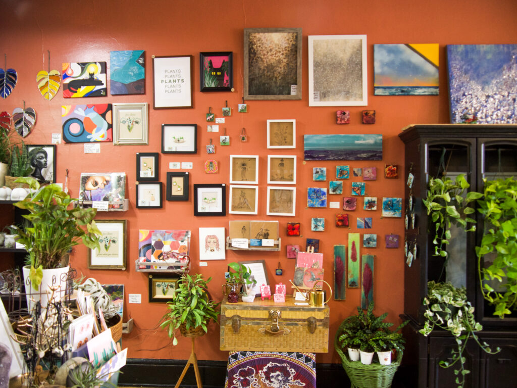 Red colorful gallery wall featuring many different paintings and green plants around it. 