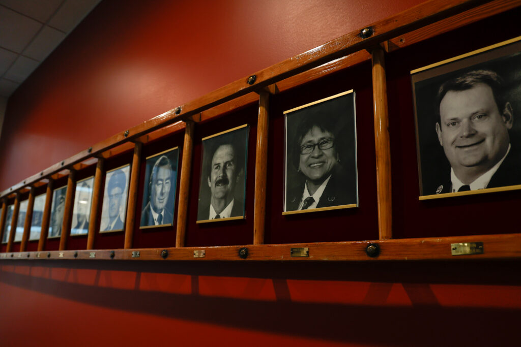 An array of picture frames on the wall of Station 1 in the Madison Fire Department, displaying many fire chiefs including Debra Amesqua. 