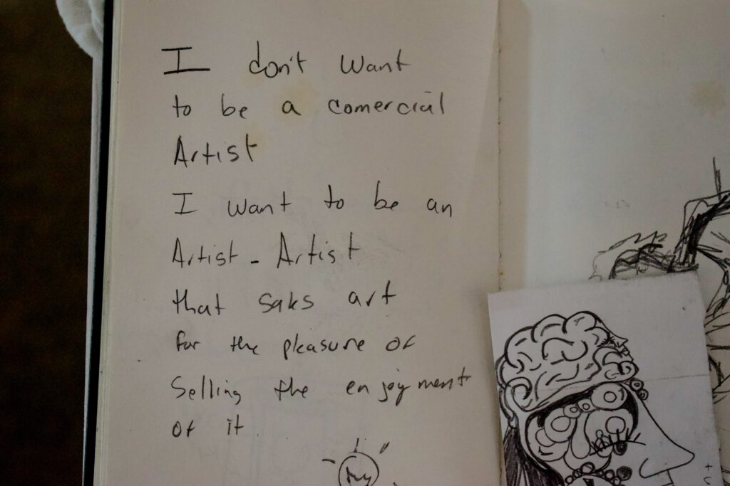 Open notebook displaying the words, “I don't want to be a commercial artist. I want to be an artist-artist that seeks art for the pleasure of selling the enjoyment of it.” 