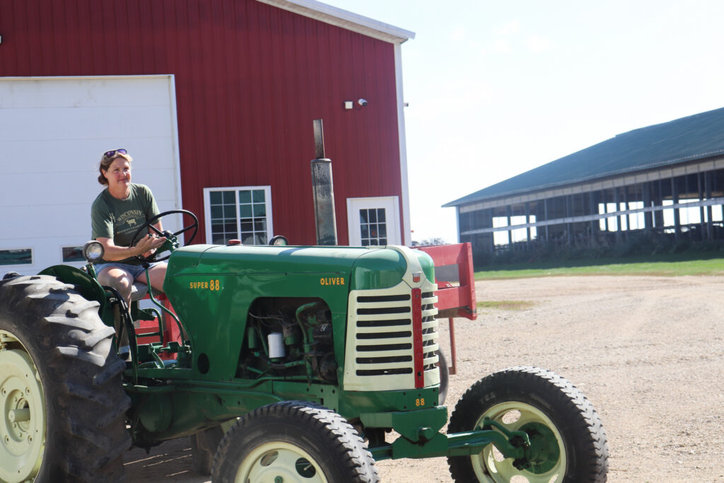 Woman drives a tractor in front of a red barn.