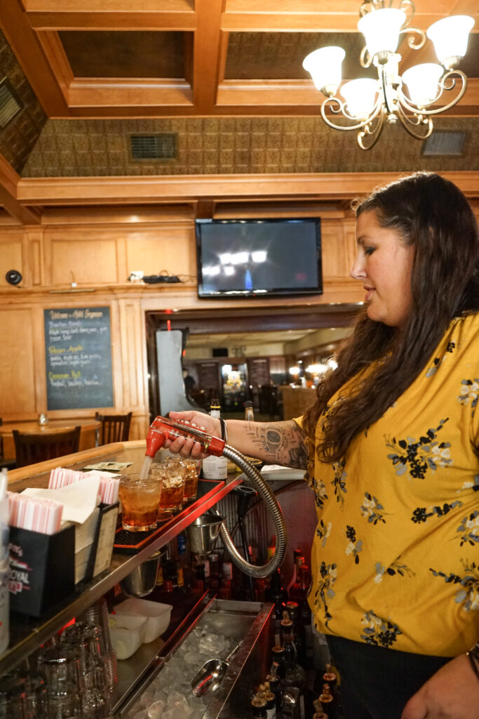 Woman uses a soda gun to prepare drinks behind a bar.