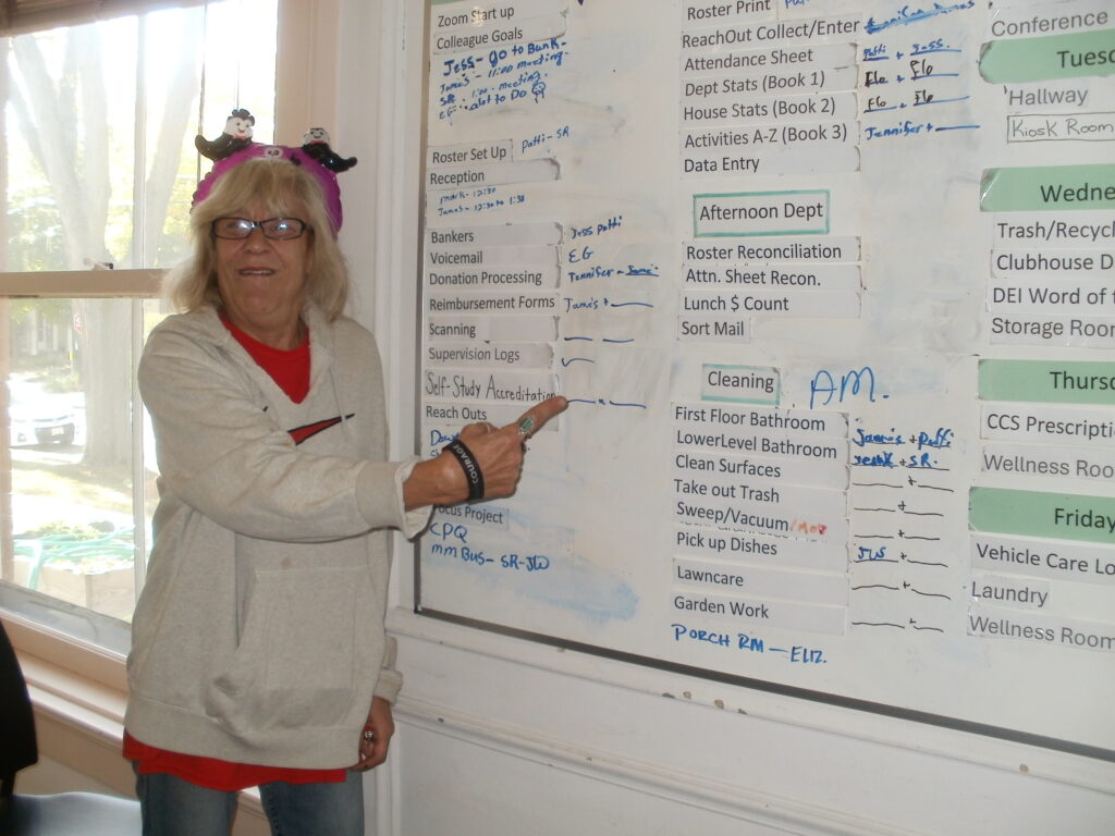 Woman stands in front of whiteboard listing tasks to be completed