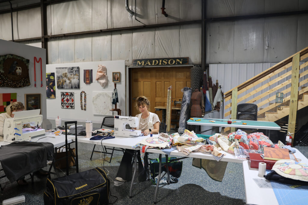 Mera Charnecki working at a sewing machine next to a pile of fabrics in the Textile Arts Center in Madison.