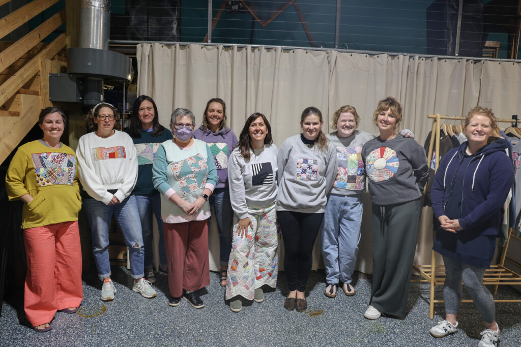 A group of students smiling with one another at the end of the workshop wearing their handmade sweatshirts. 