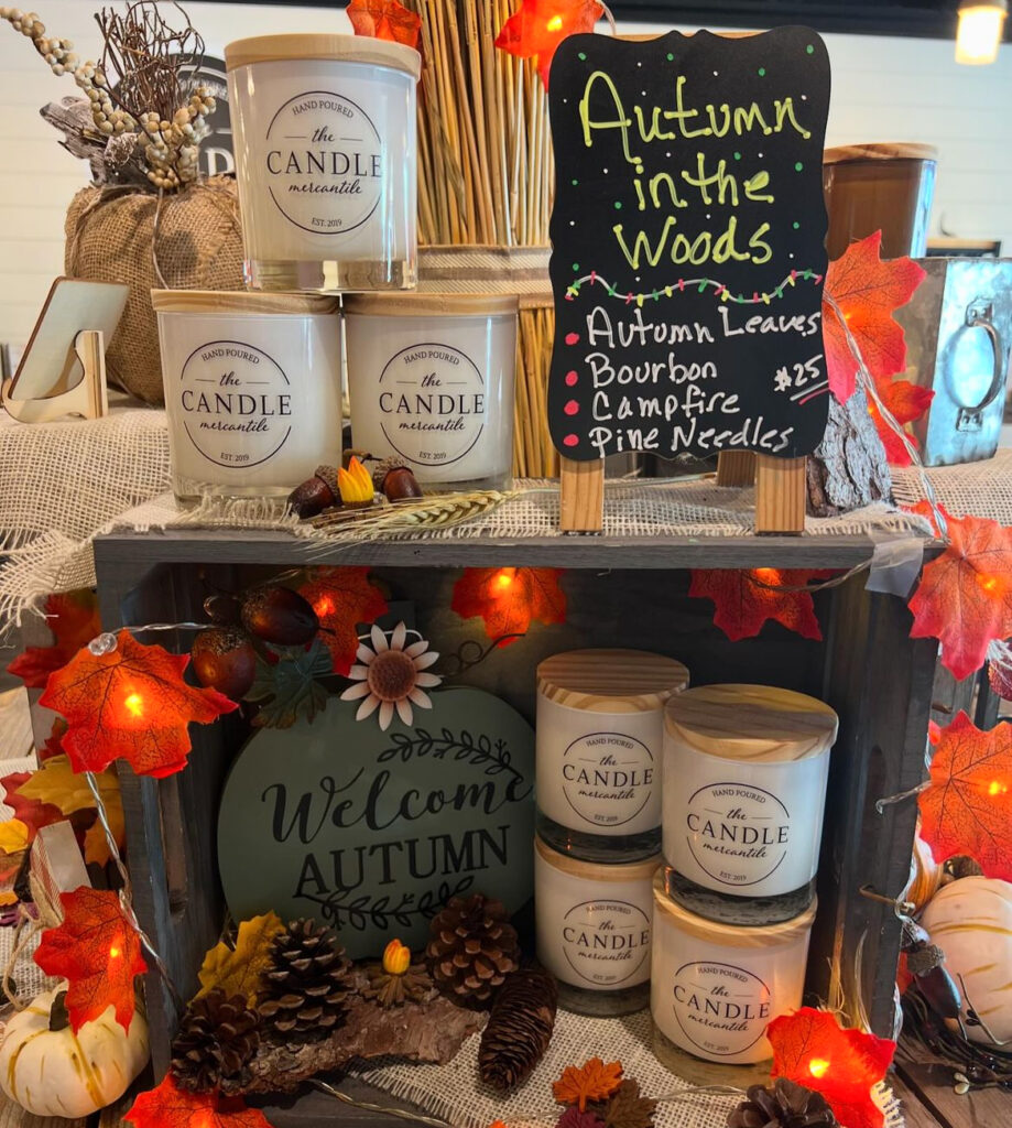 A display of candles sits next to a sign that says "Autumn in the Woods" and lists the scents of the candles.