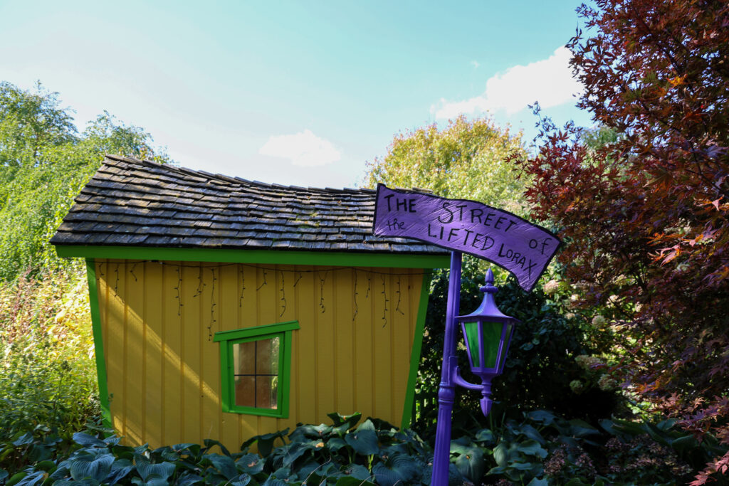 A yellow building near a sign that reads, "The Street of the Lifted Lorax," in Bookworm Gardens.