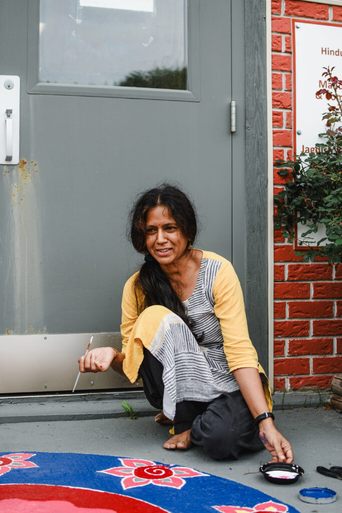 A woman sitting against a metal door and brick wall painting the on the ground.