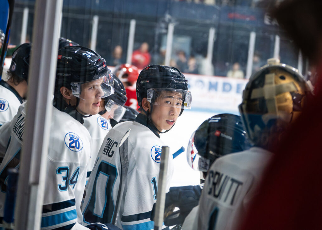 Tang, surrounded by fellow players, looking behind his shoulder standing along the ice.