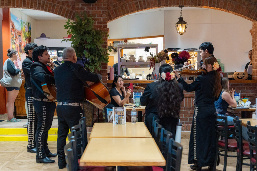 Mariachi band performing around a woman's table.