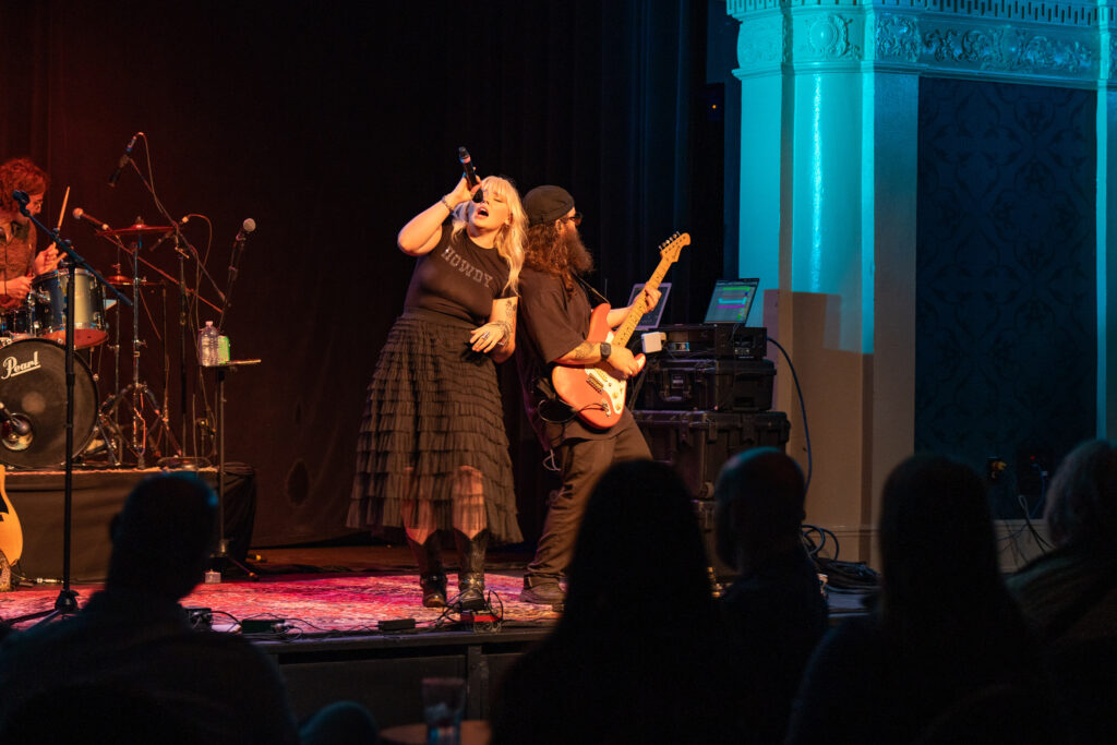 Heyward singing on stage leaning against her guitarist.