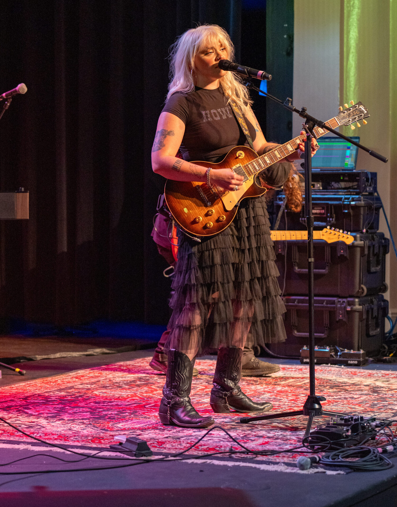 Heyward, wearing all black and cowboy boots, singing into the microphone with guitar in hand.