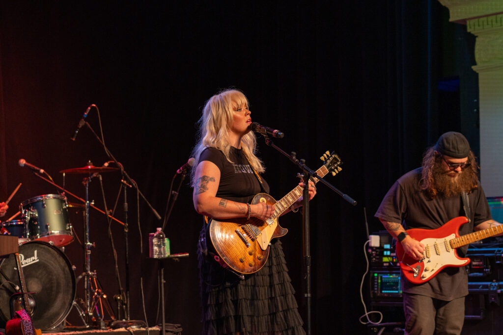 Heyward singing into the microphone while strumming an electric guitar