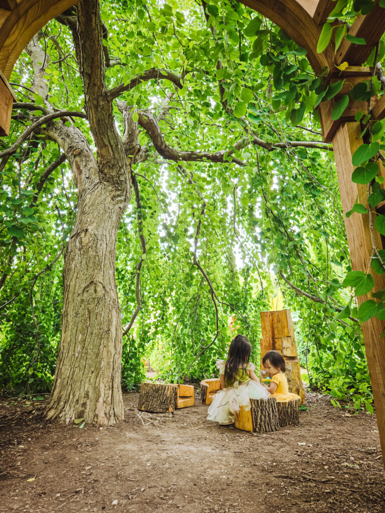 Two children play under a tree in Bookworm Gardens.
