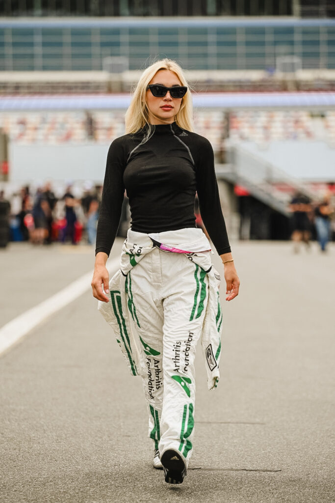 Woman racer with uniform walking with bleachers in the background