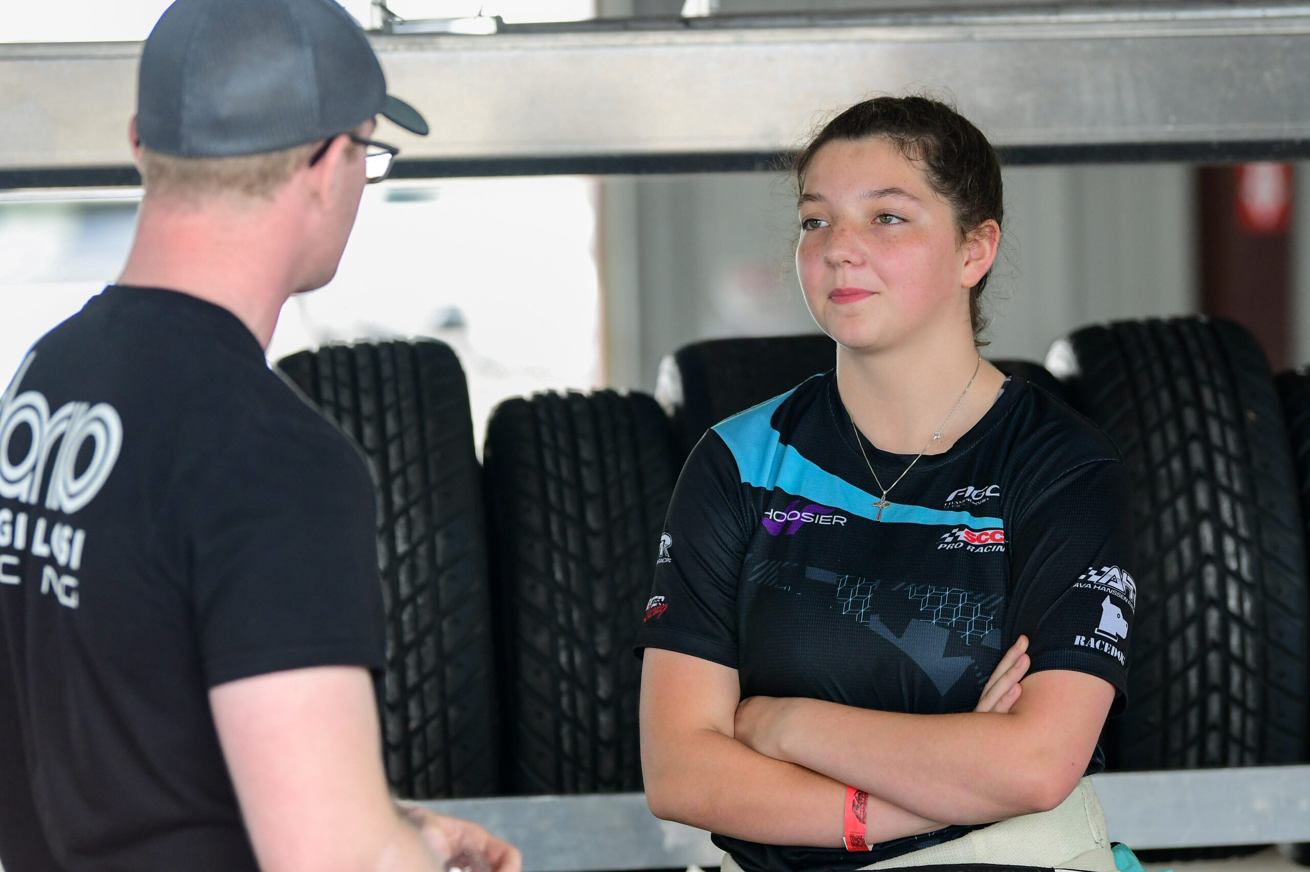 Ava Hanssen standing in front of tires with her arms crossed, talking to a man.