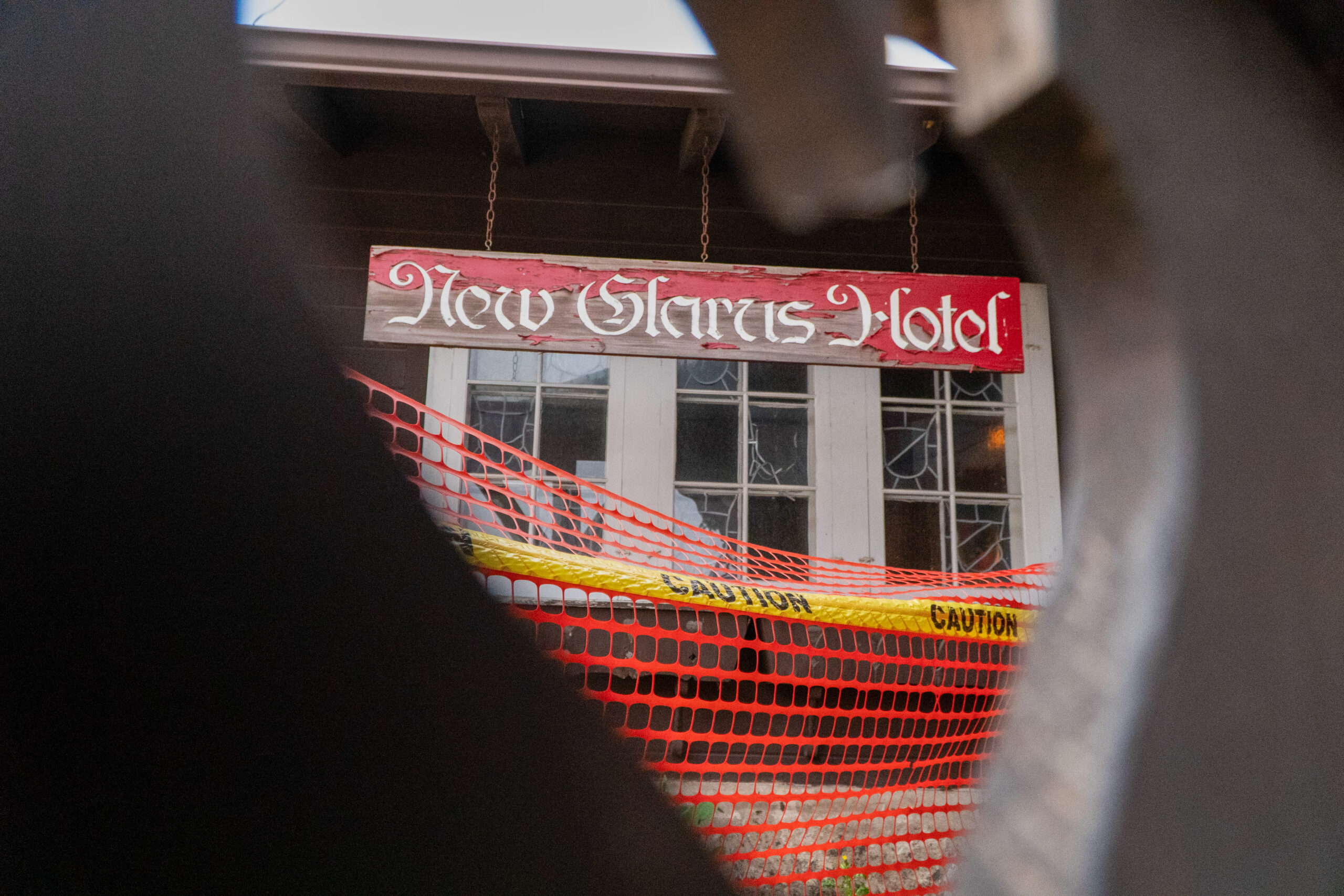 Faded New Glarus Hotel sign with chipped paint stands behind caution tape and temporary construction fencing.