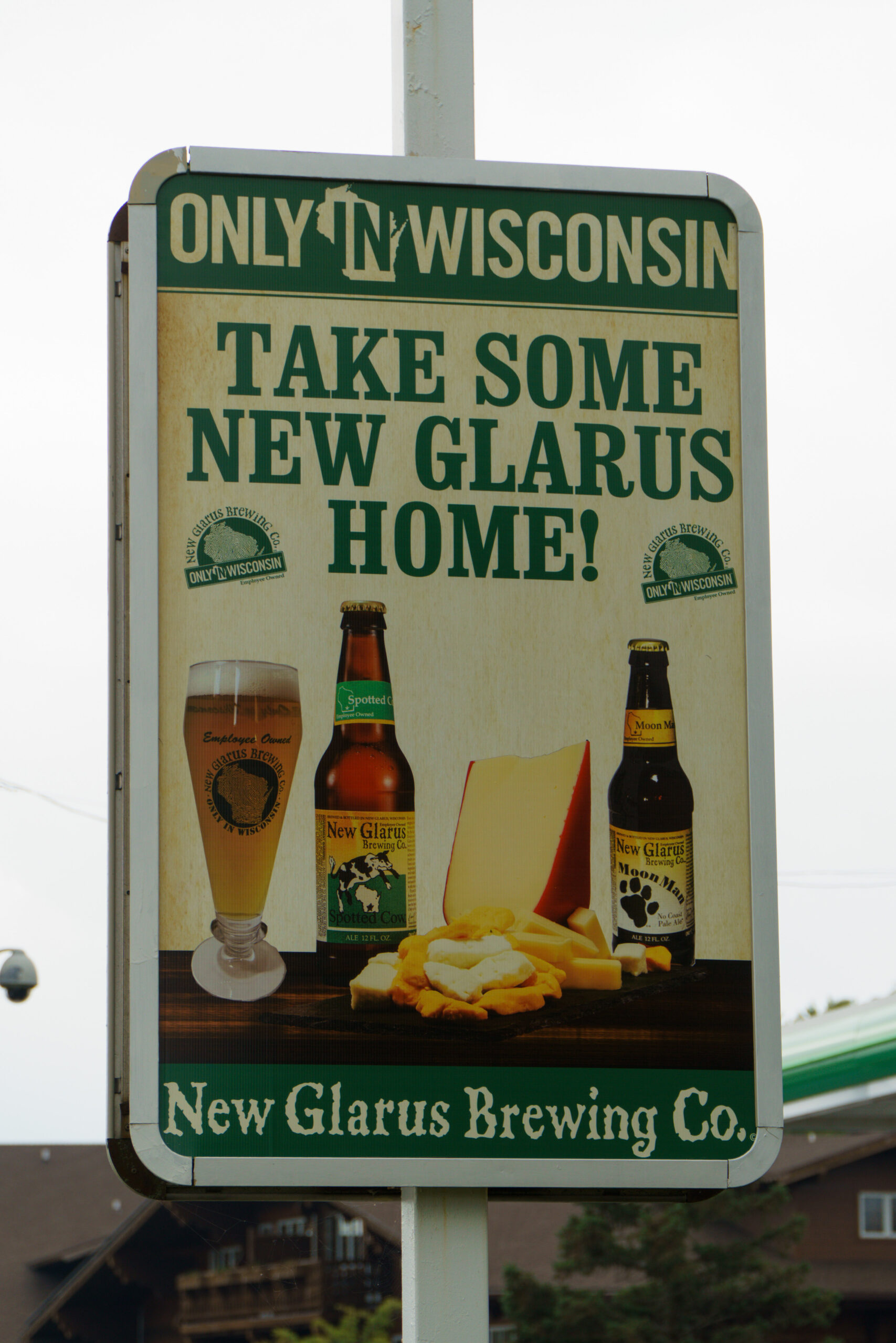 Vintage New Glarus Brewing Company street sign reading “Only in Wisconsin, Take Some New Glarus Home!” with images of beer bottles and cheese products.