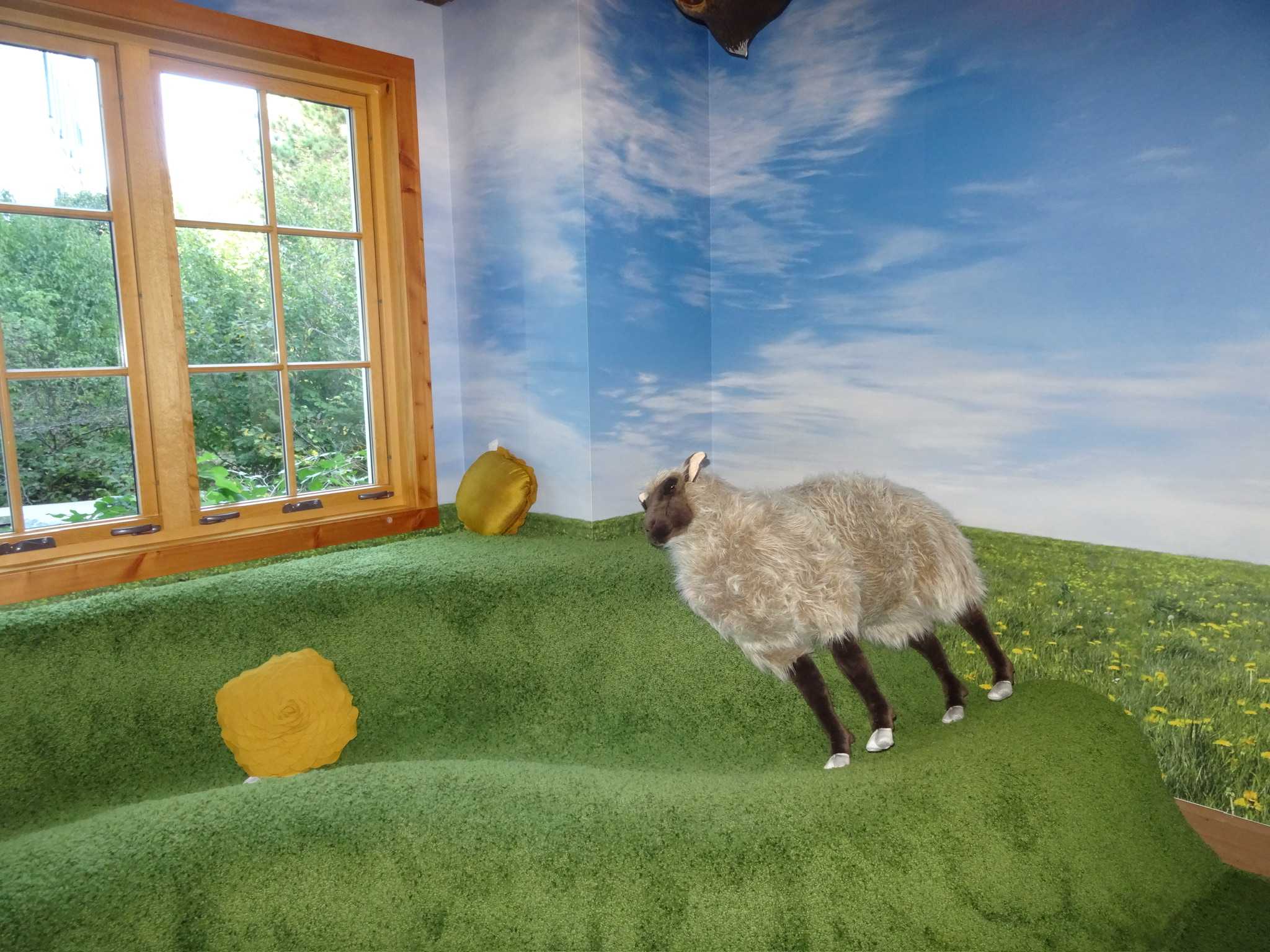 Statue of a sheep lays on grass turf inside.