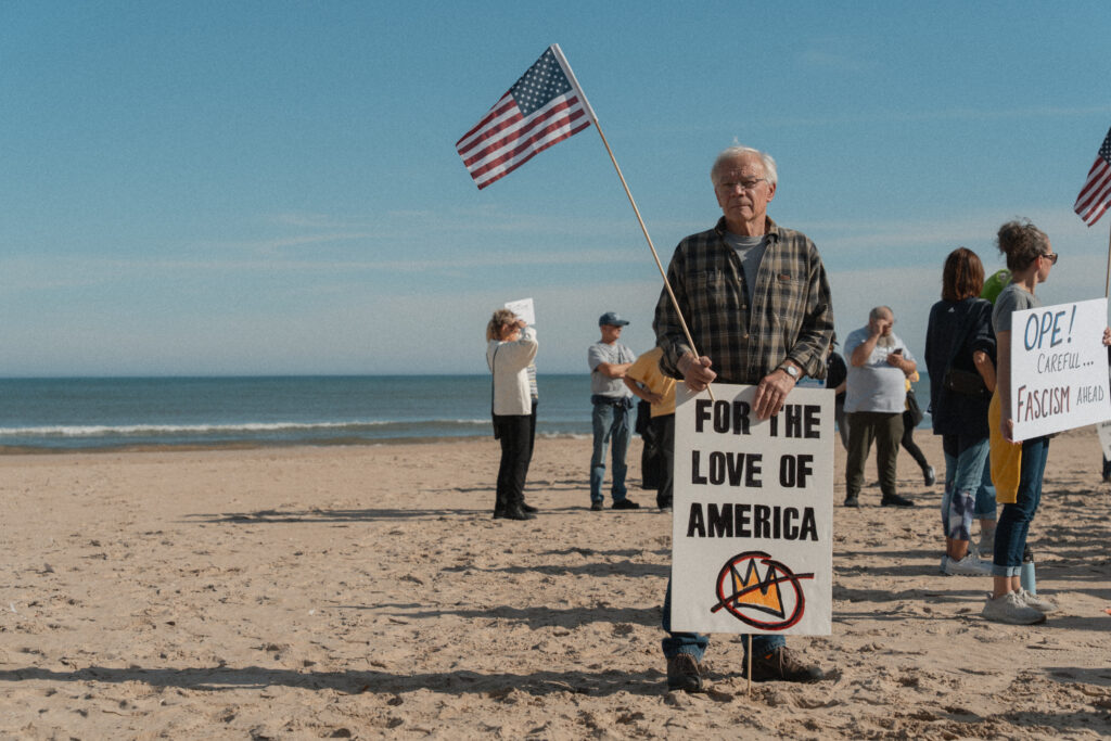 man poses with a sign that says "for the love of America" and an American flag.