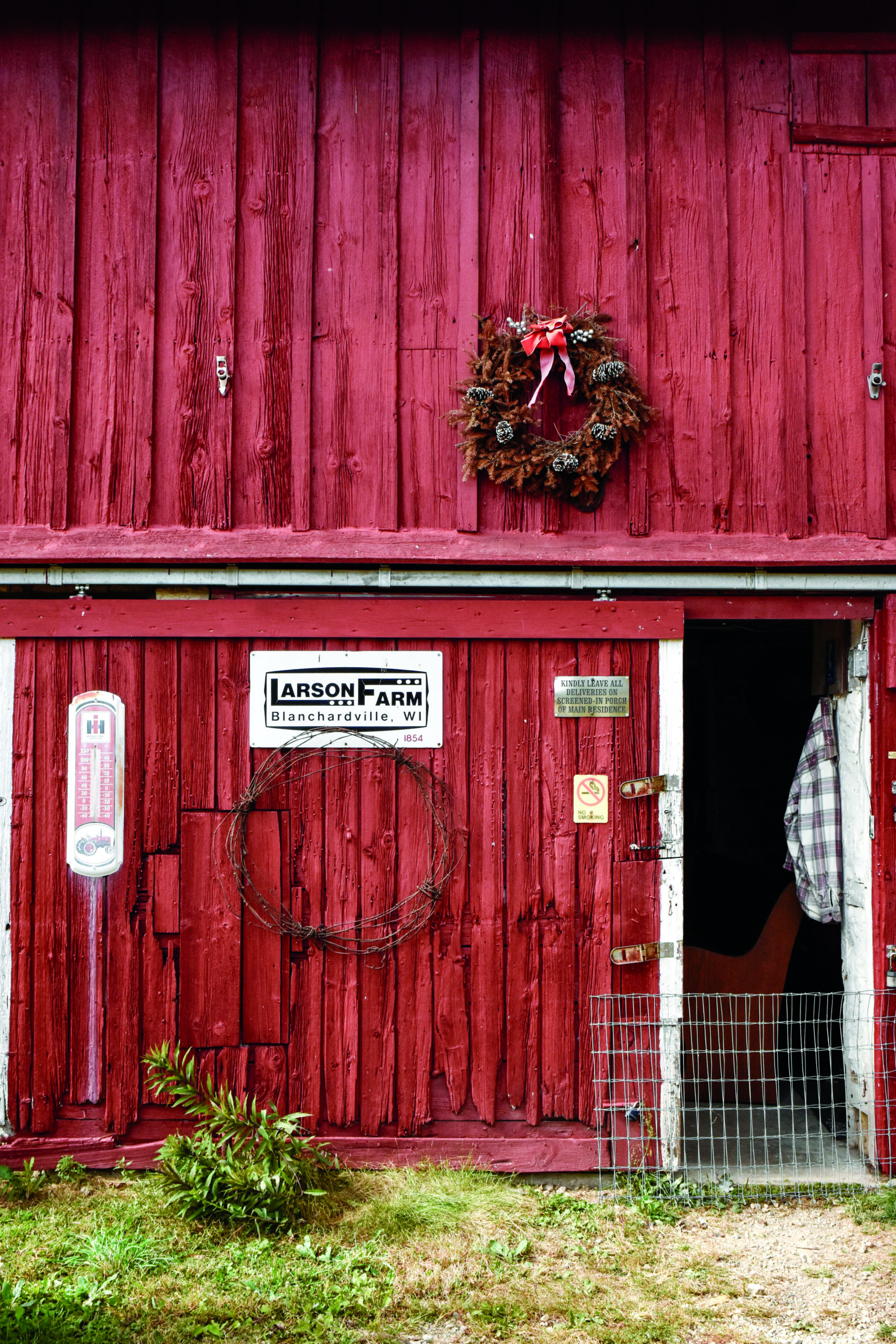 Large red barn door slightly open with 'Larson Farm' sign and a wreath hanging on it.